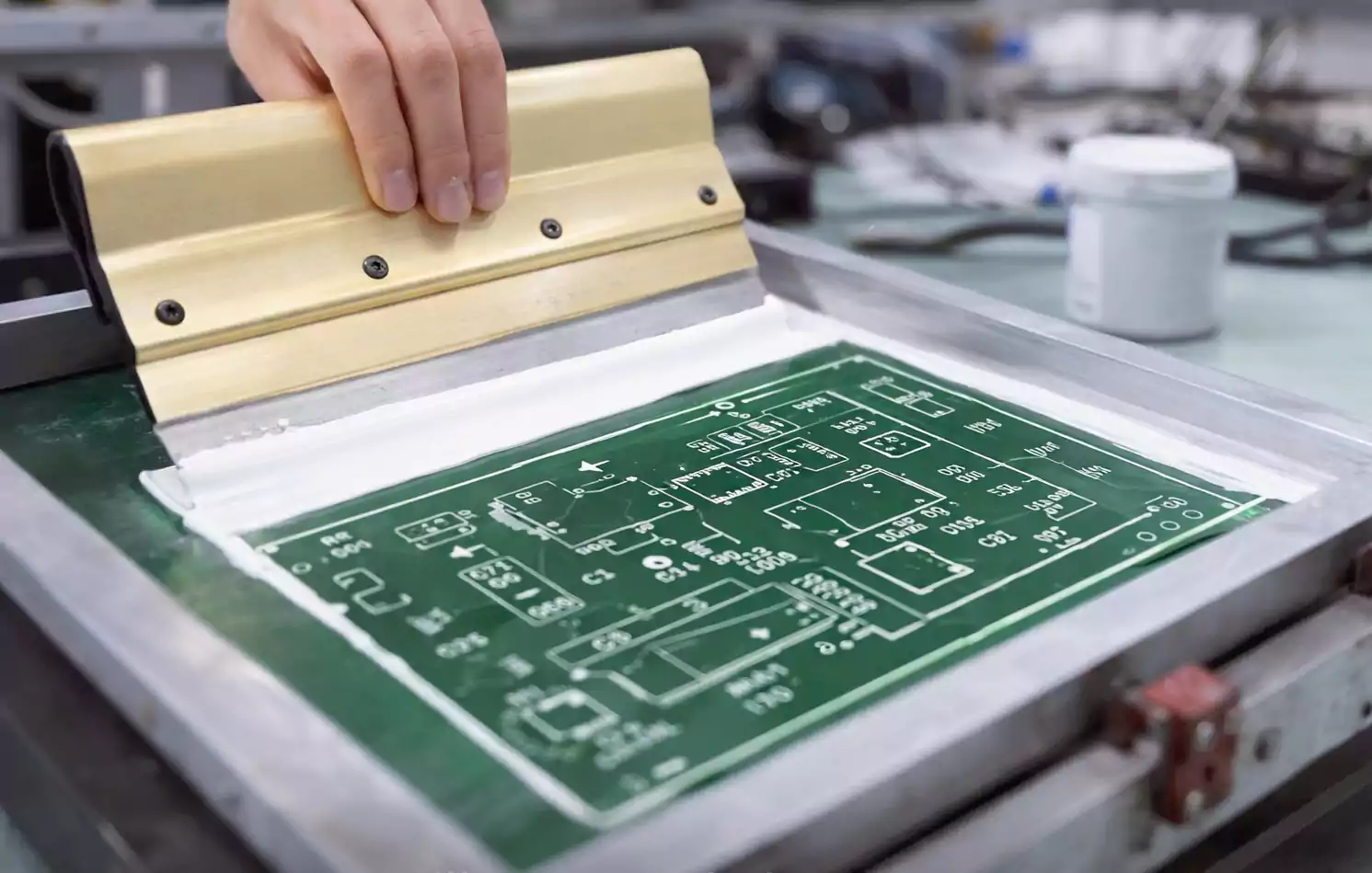 Technician using a squeegee to screen print white legend on a green PCB panel.